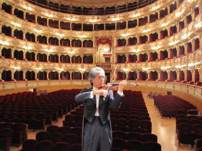 コンサートホールを背景にバイオリンを演奏する八嶋博人